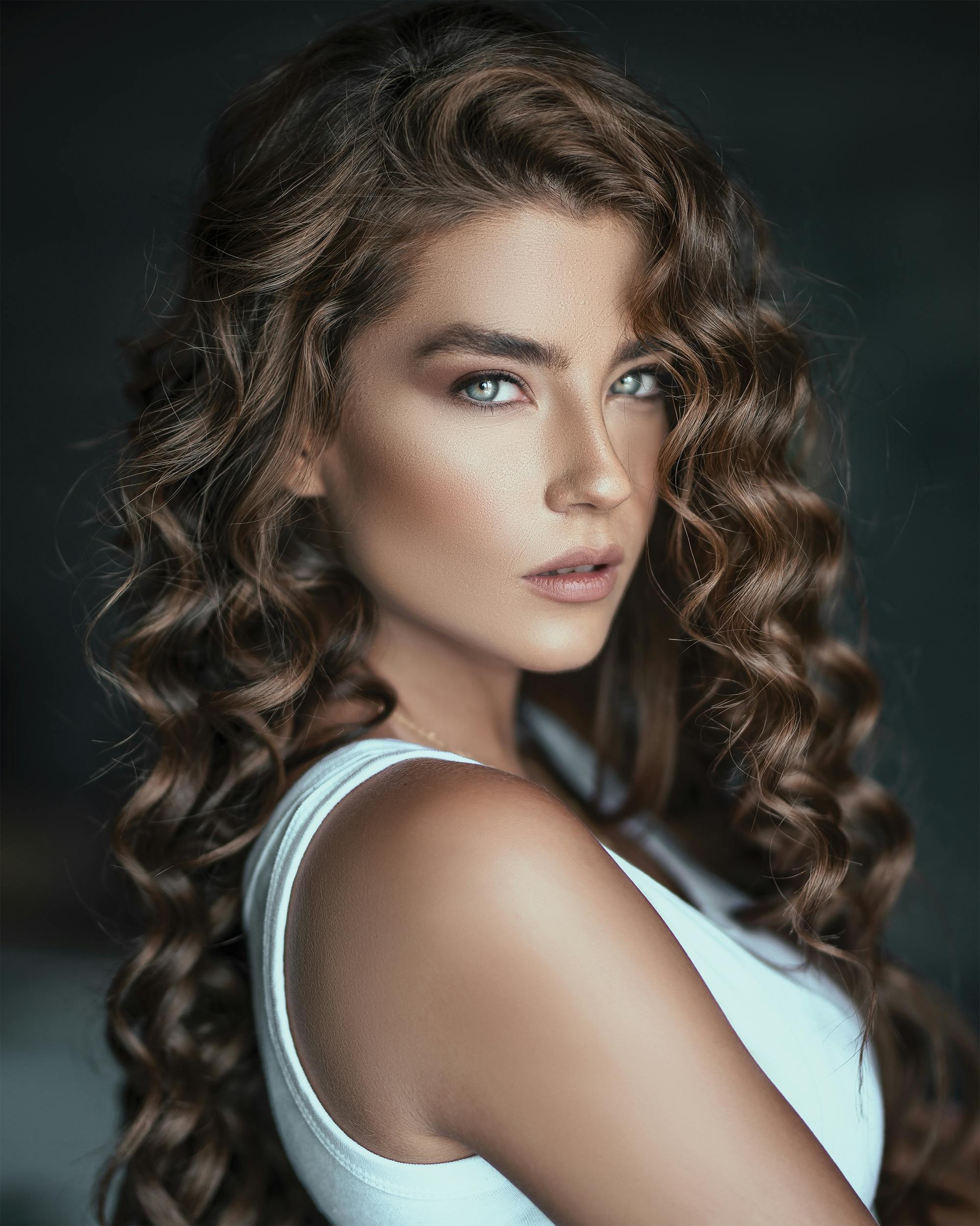 A striking portrait of a woman with luscious curly hair and a fierce expression in a white top.