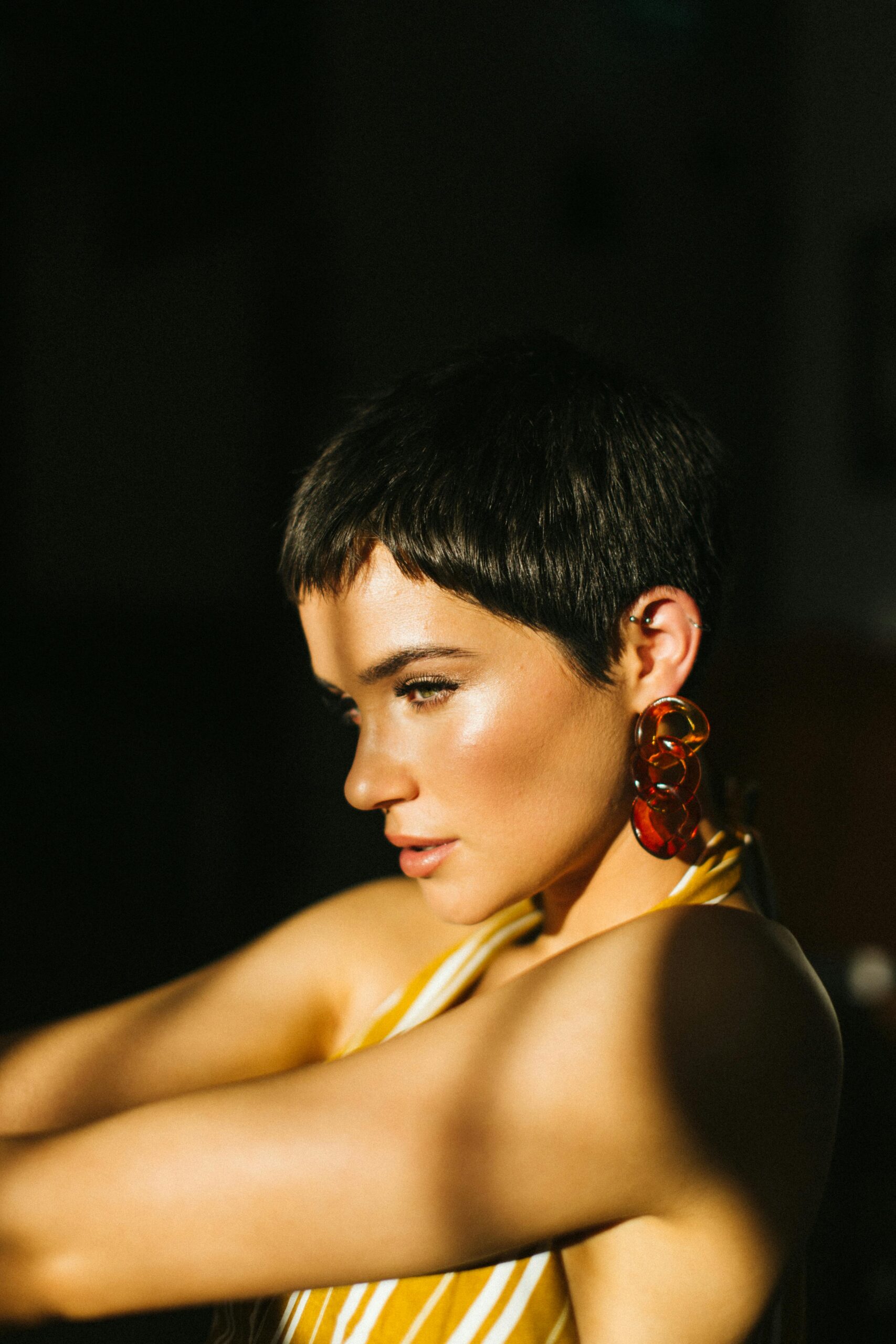 Woman with short hair and bold earrings posing indoors in stylish lighting.